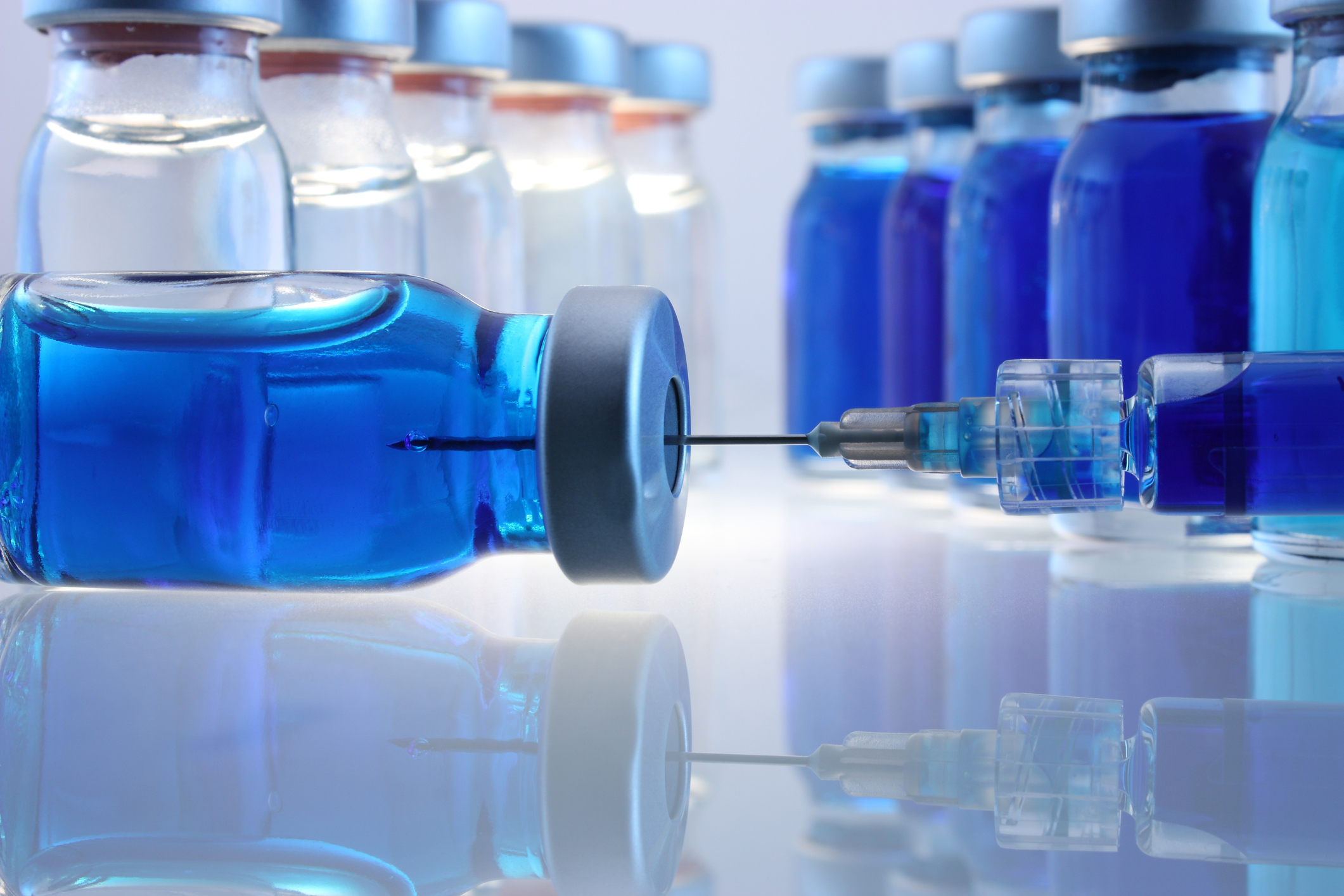 Rows of glass vials and a syringe inserted into one.