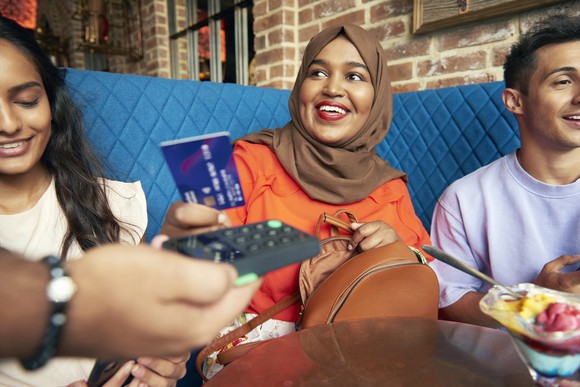 A woman wearing a hijab sitting with a man and a woman at a restaurant and paying with a credit card/