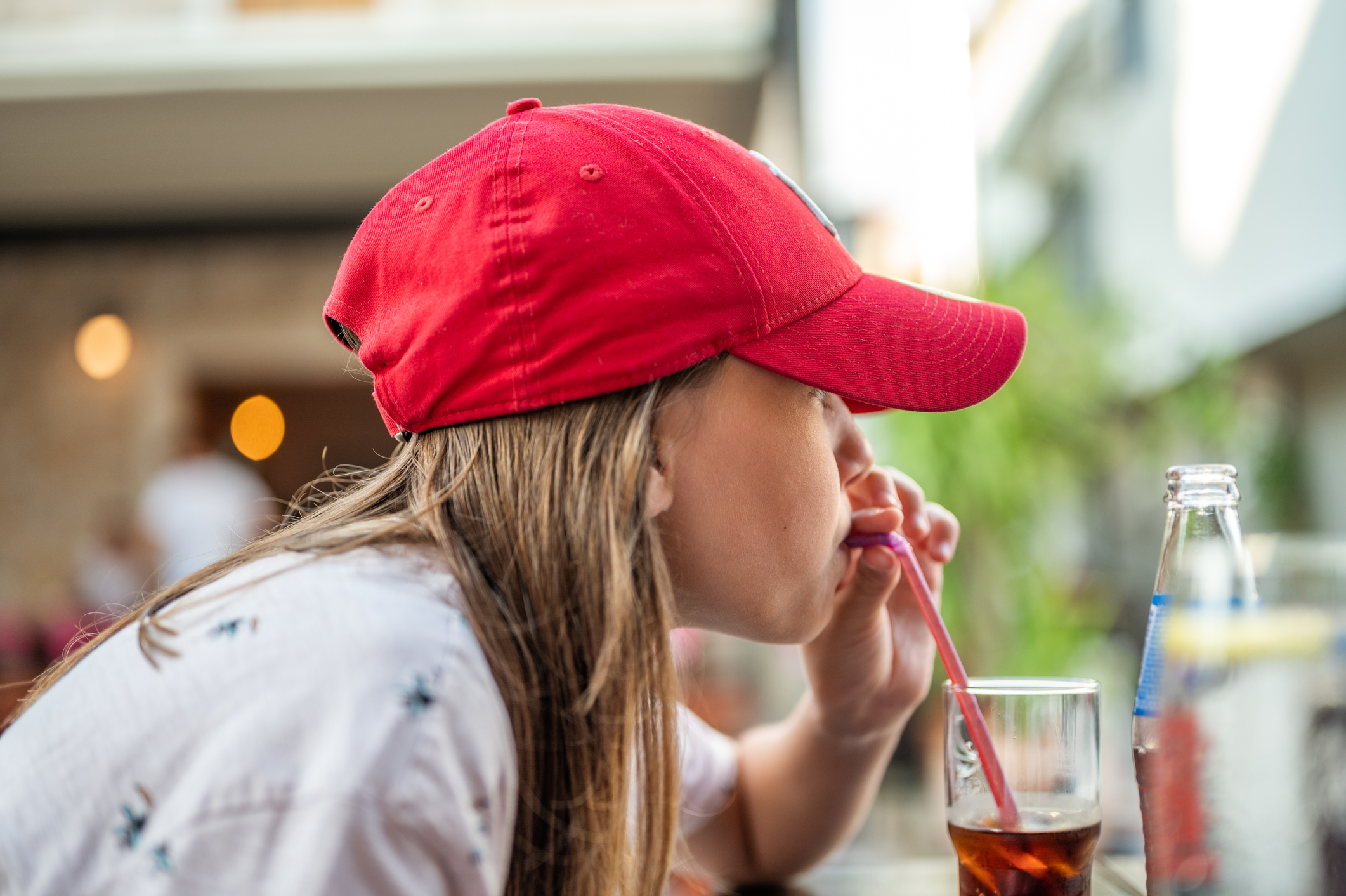 Person in red hat drinking from a glass of cola with a straw.