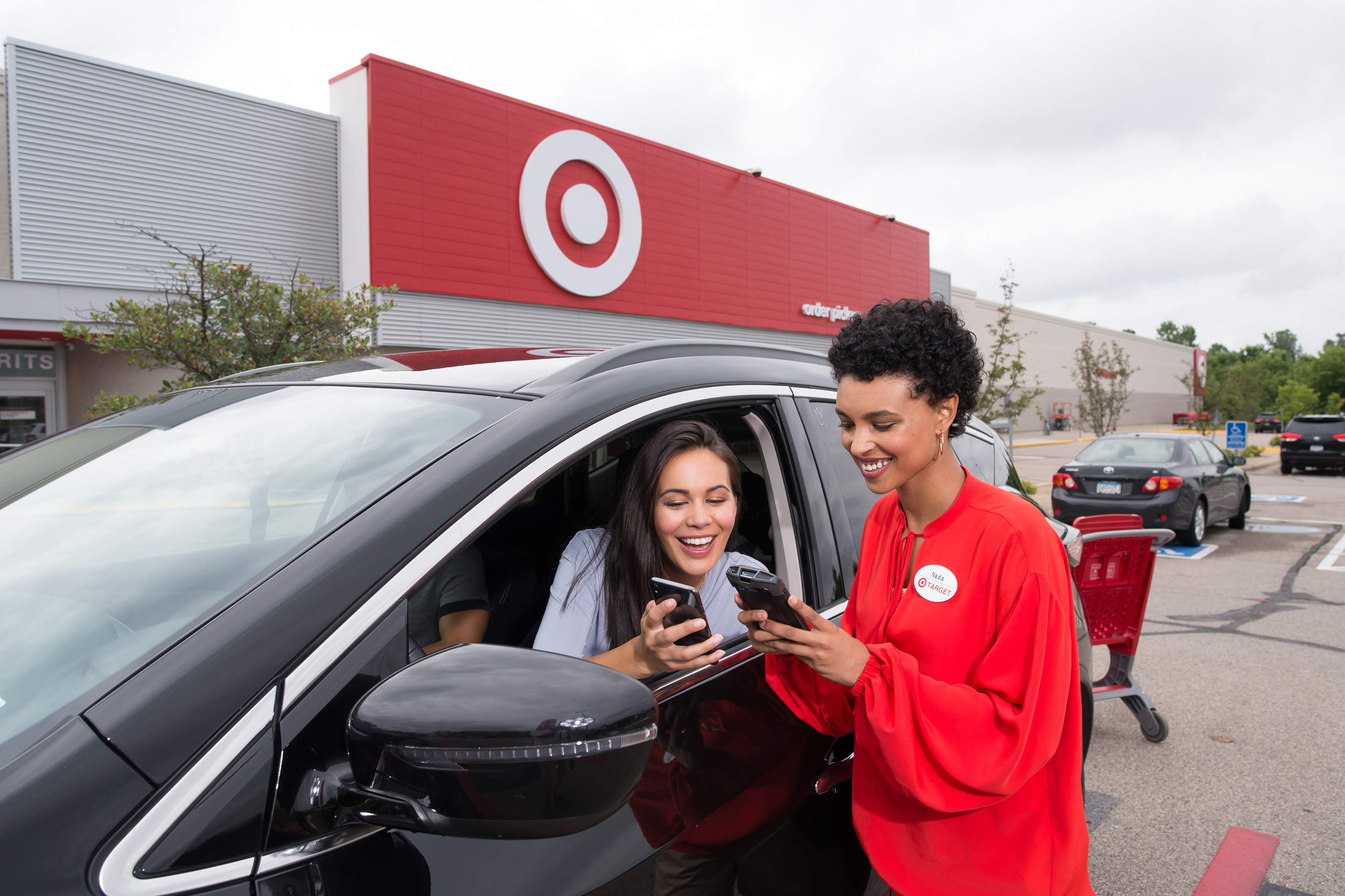 A Target team member looking at phones with a drive-up customer in a car.