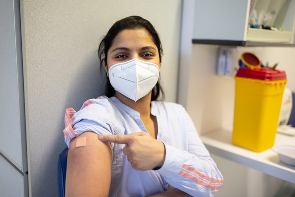 Young person proudly pointing at their upper arm where a vaccine shot was given. 