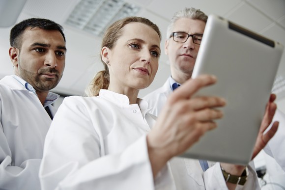 Three people in medical attire looking at a tablet.