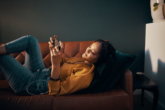 A woman plays a game on her phone while reclining on a couch.