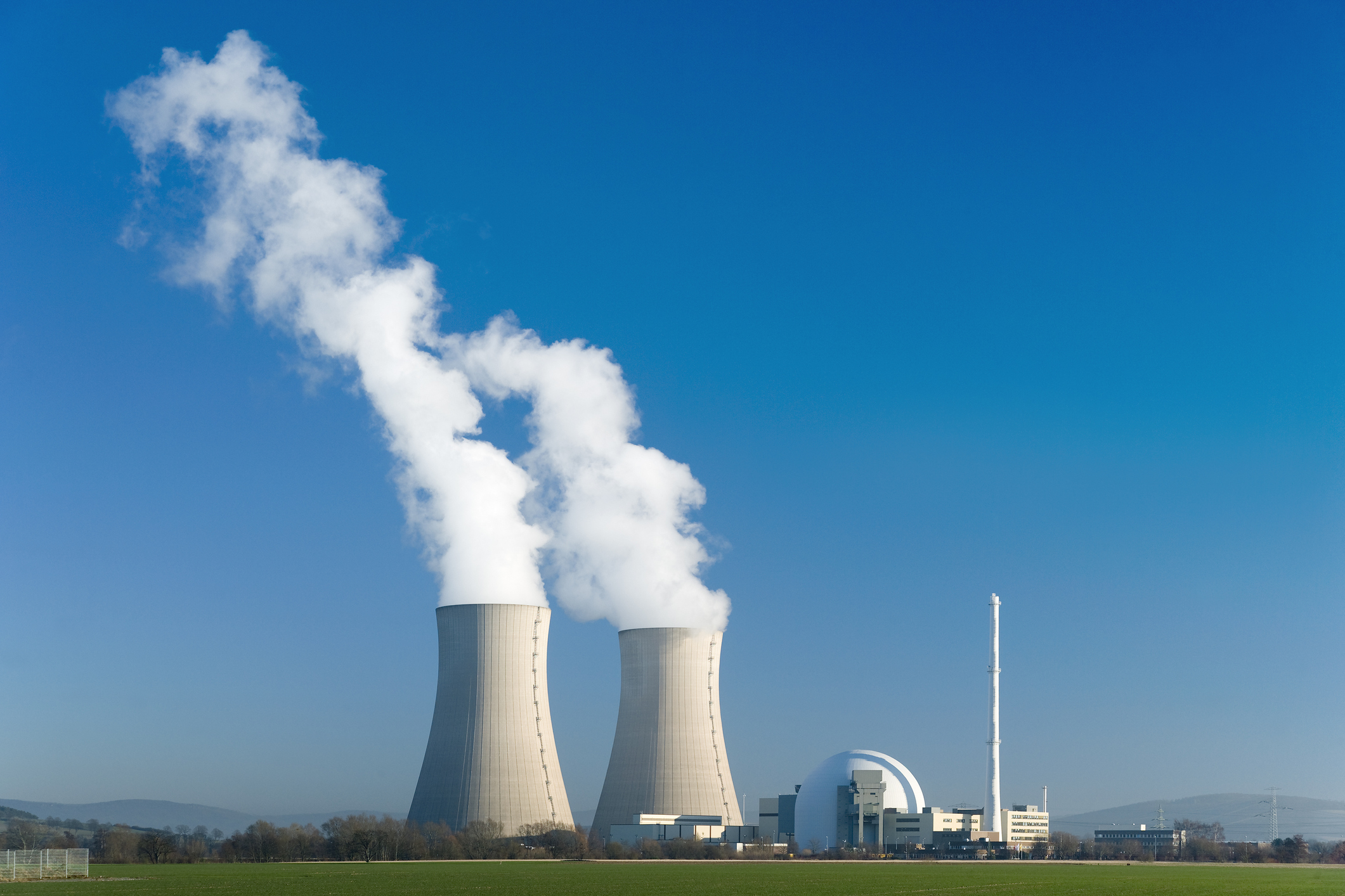 Nuclear power station with two steaming cooling towers in blue sky.
