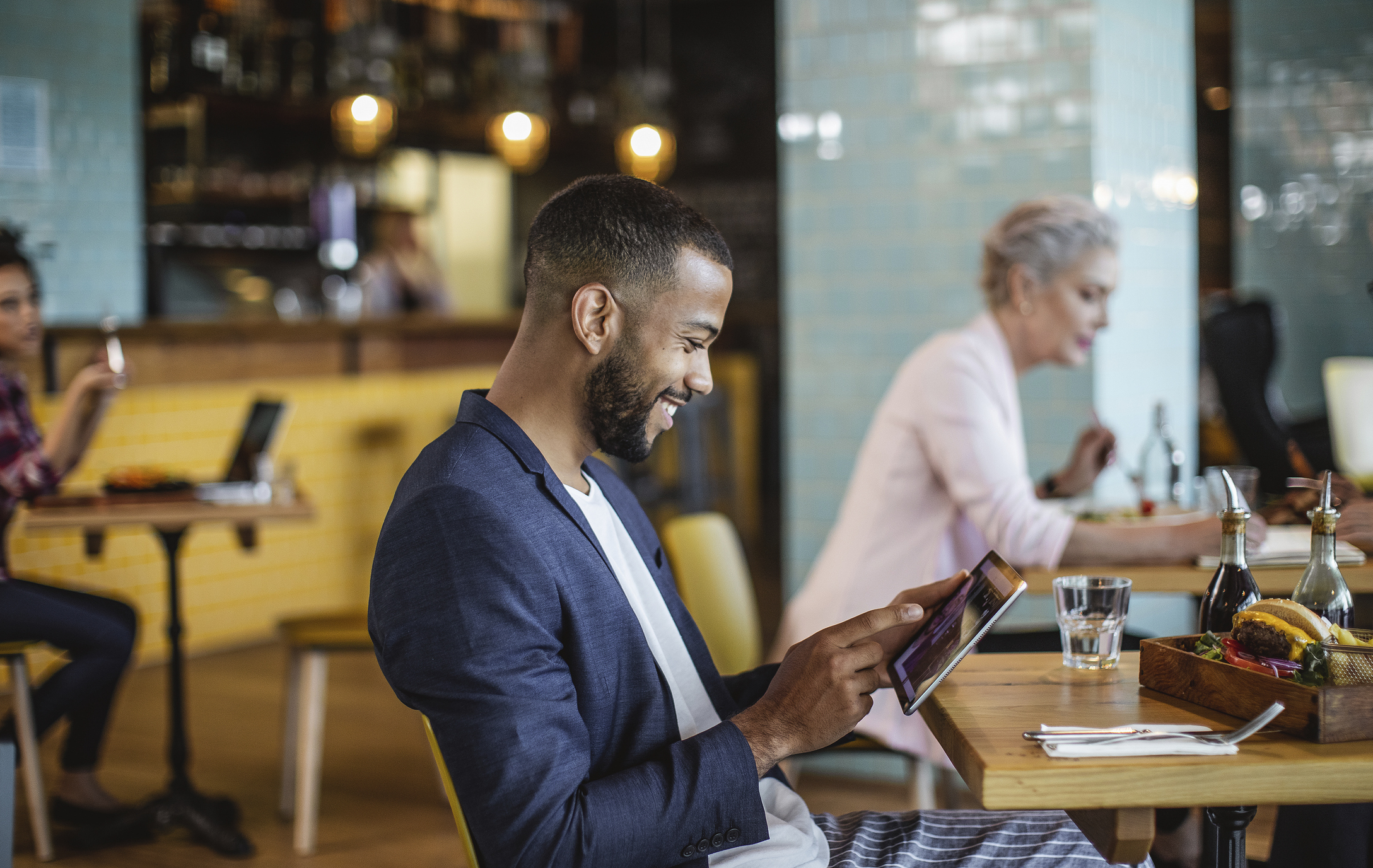 Smiling business person in coffee shop looking at tablet.
