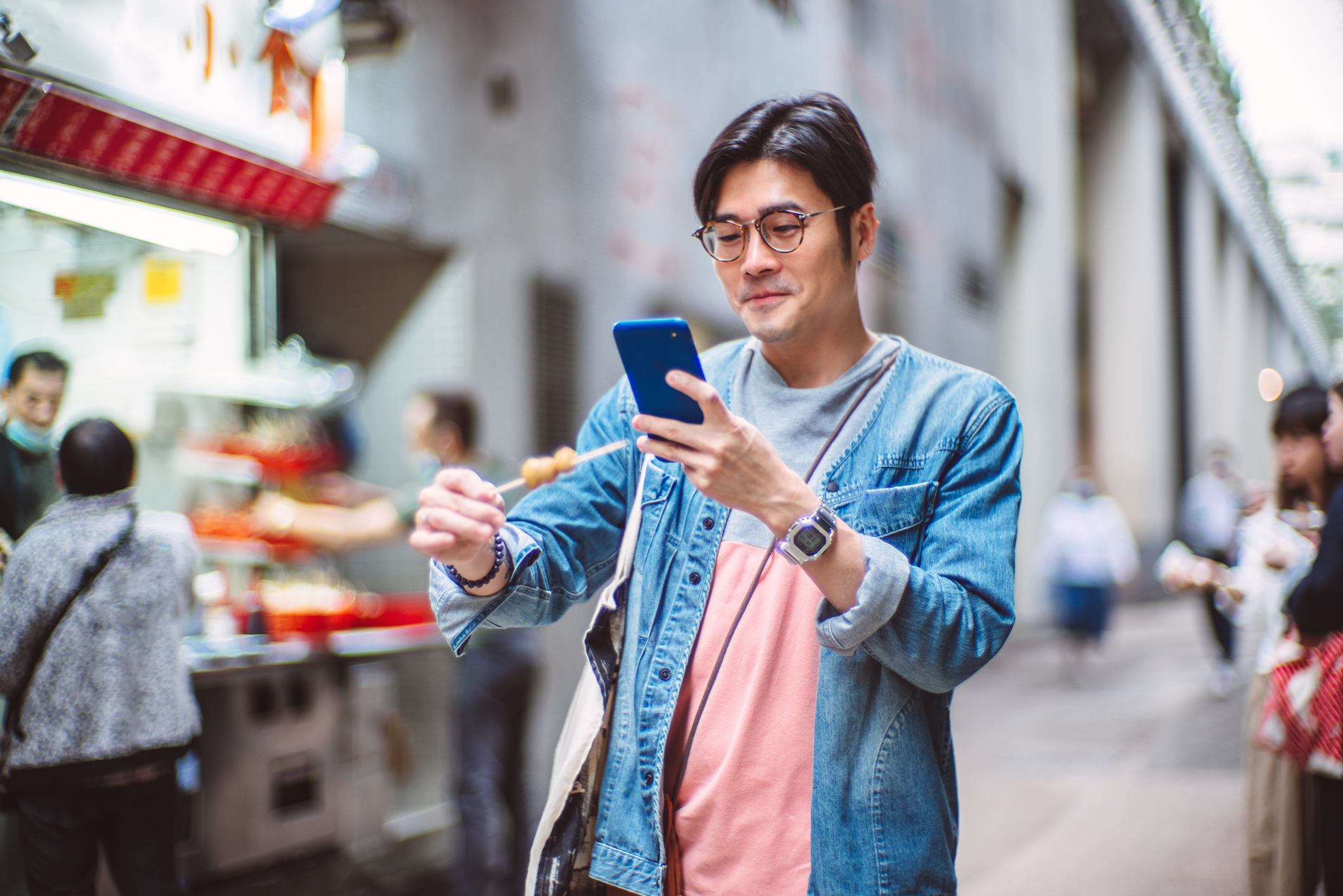 A person holds their smartphone to take a picture of the food on a stick they are holding.