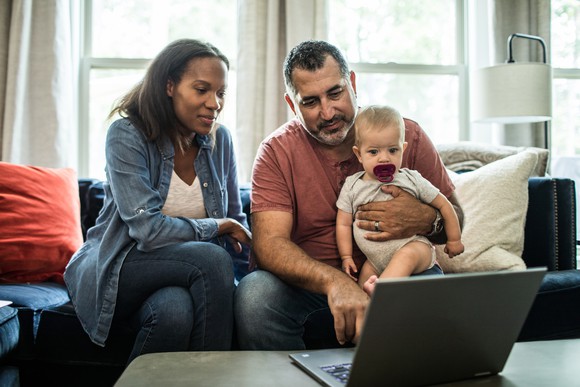 Two people looking at laptop together while one holds baby