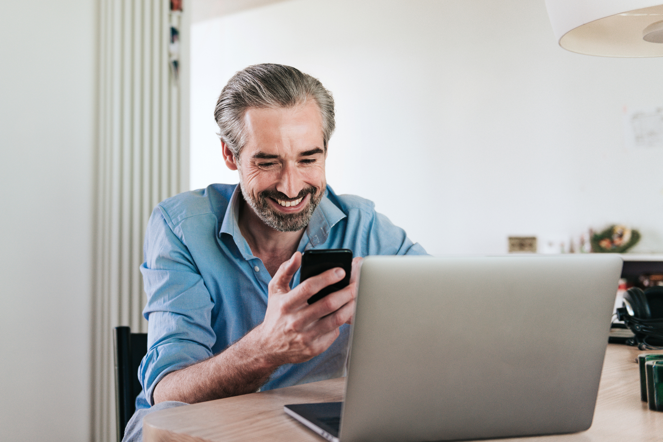 Person smiles while sitting down and look at phone and laptop screen.