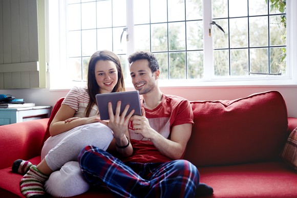 A young couple sitting on a sofa and looking at a tablet computer.