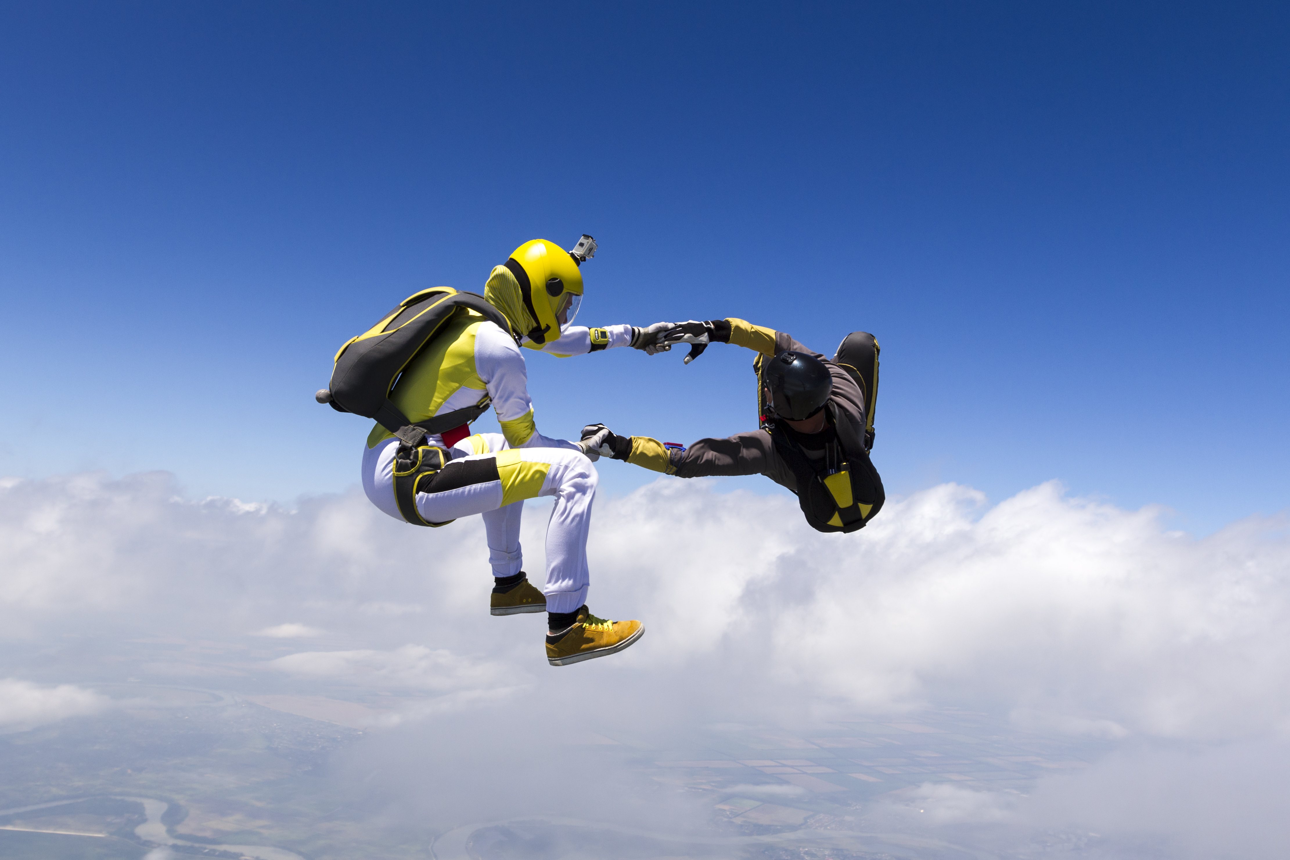 Two people holding hands while skydiving against the backdrop of a bright blue sky.