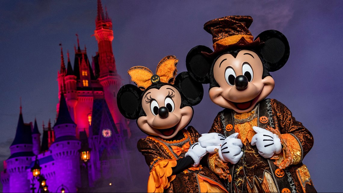 Mickey and Minnie Mouse wearing Halloween costumes in front of the Magic Kingdom castle.
