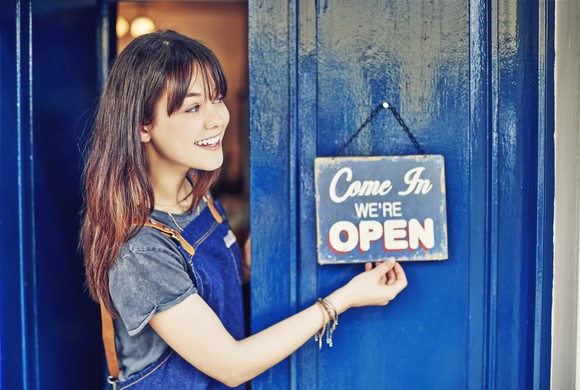 A smiling business owner hanging an open sign on their blue shop door
