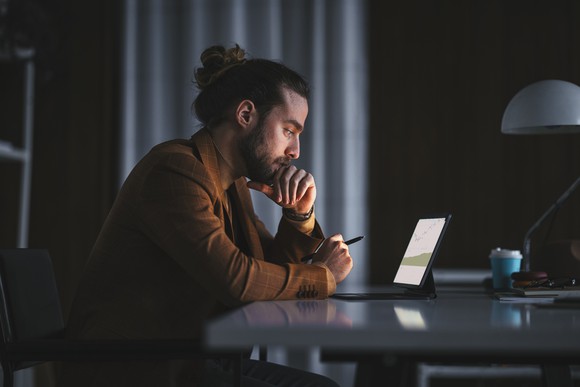 A person with an open laptop intently focuses on a chart. 