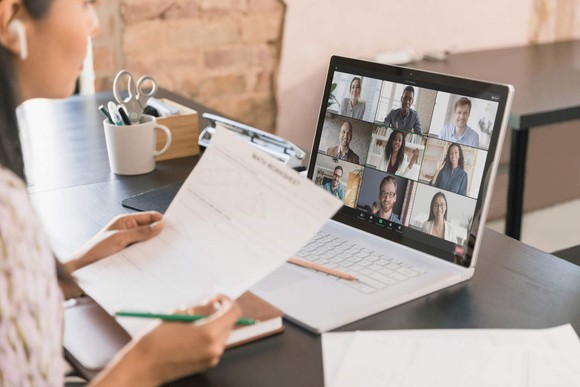 A person attends a meeting on Zoom while reviewing sheets of paper.