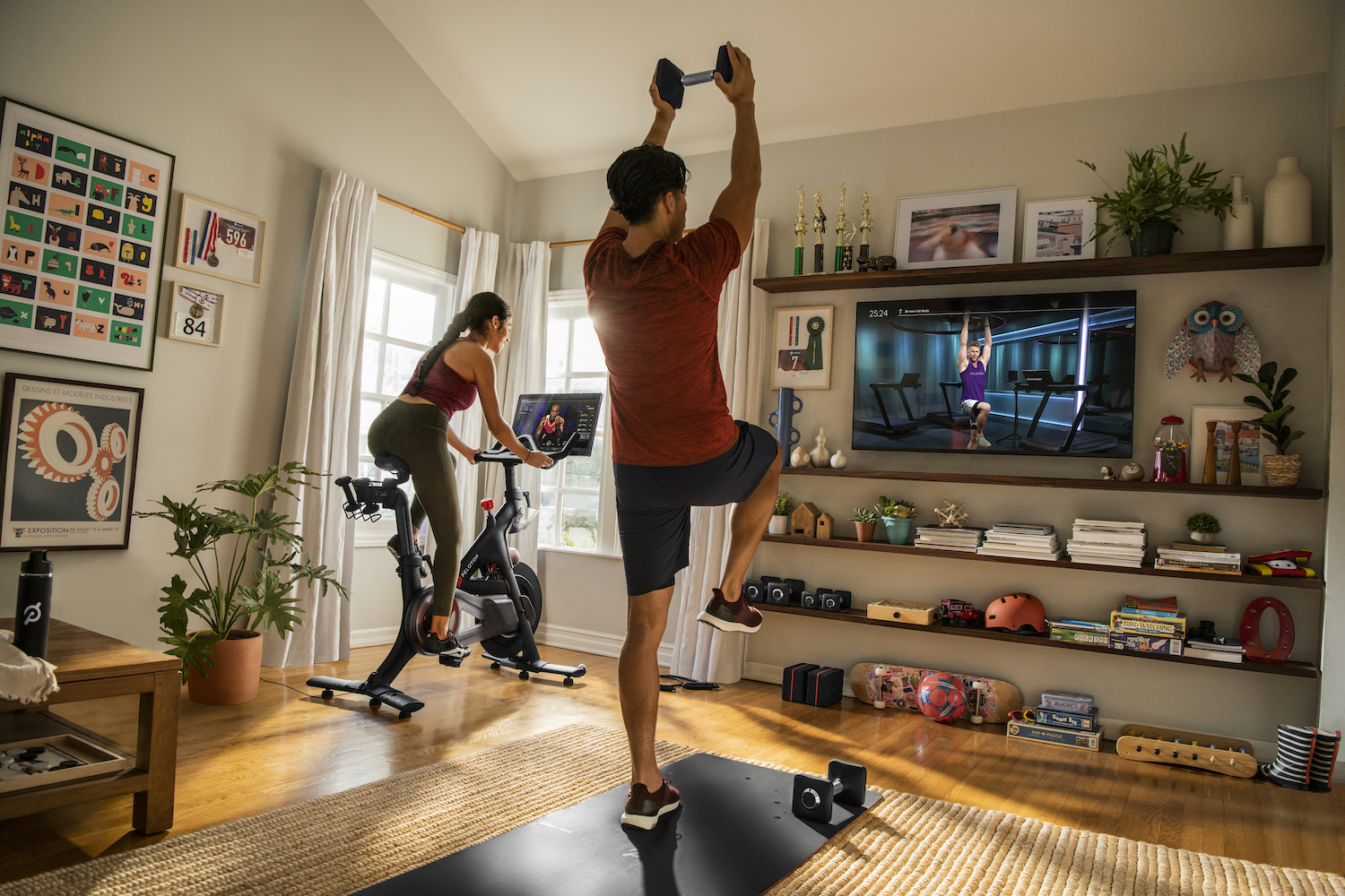 Two people exercise while viewing fitness content from Peloton.