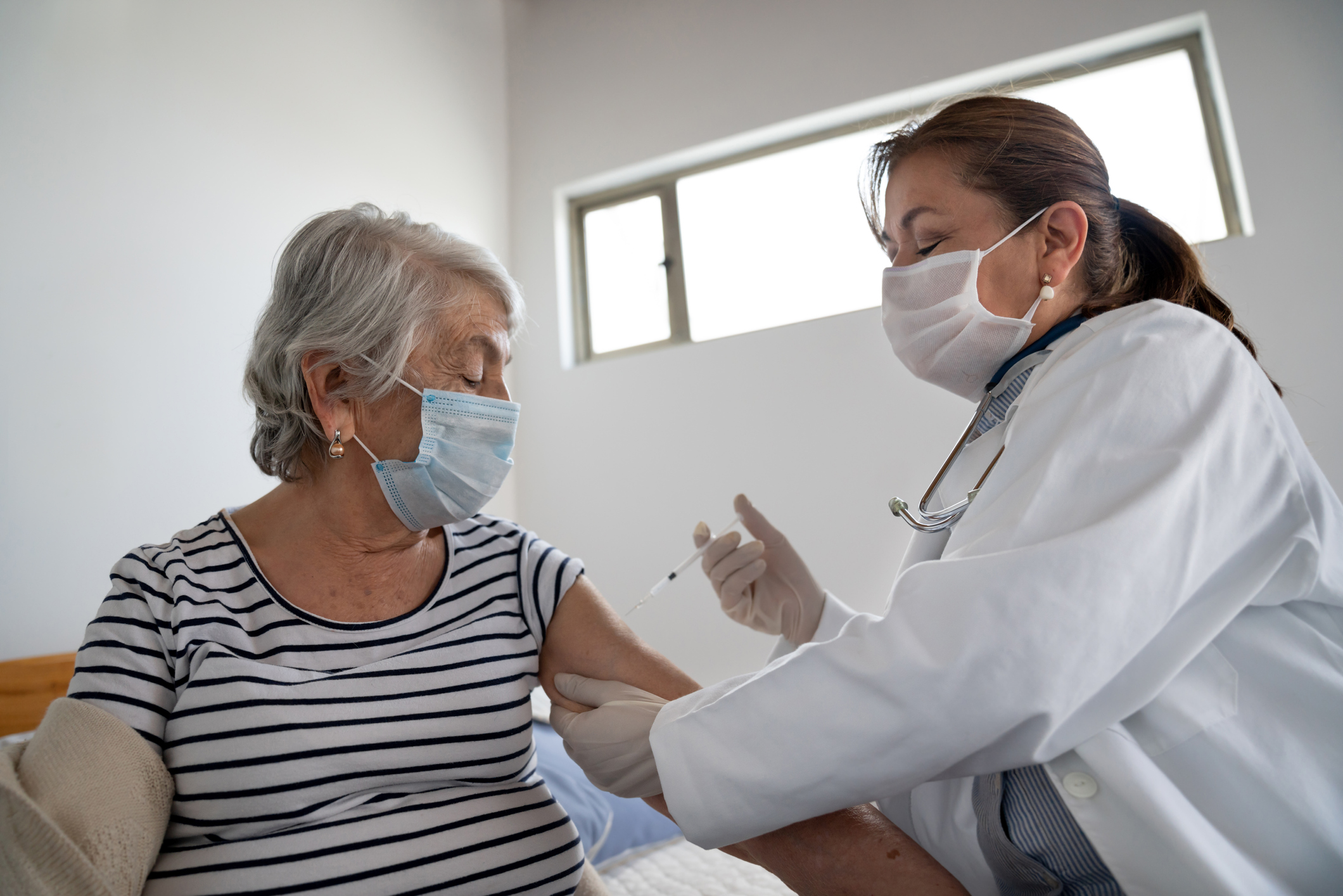 A person getting a vaccination from a clinician wearing a COVID mask.