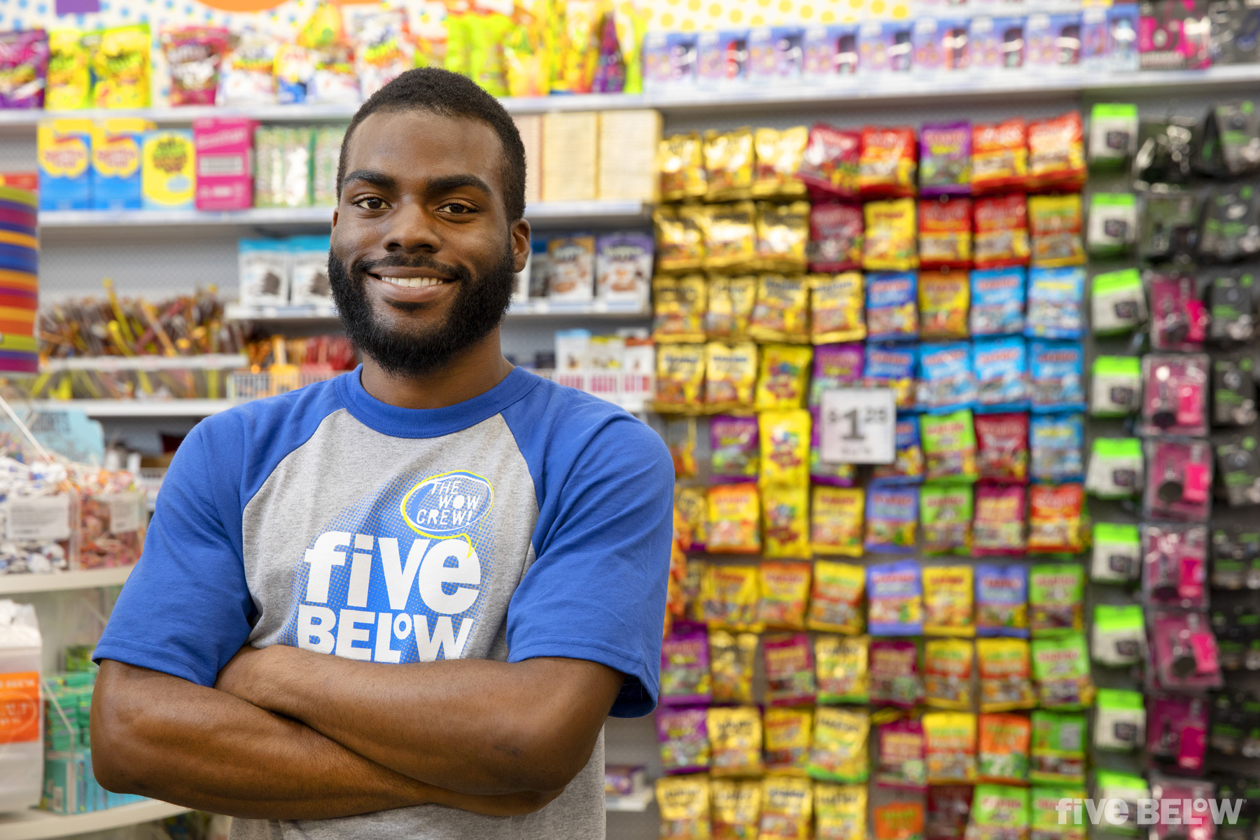 An employee of Five Below smiles with arms crossed in a store location.