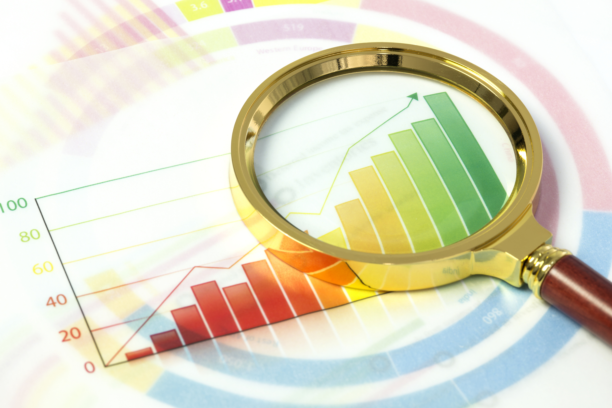 A magnifying glass lies on a colorful stock market data chart.