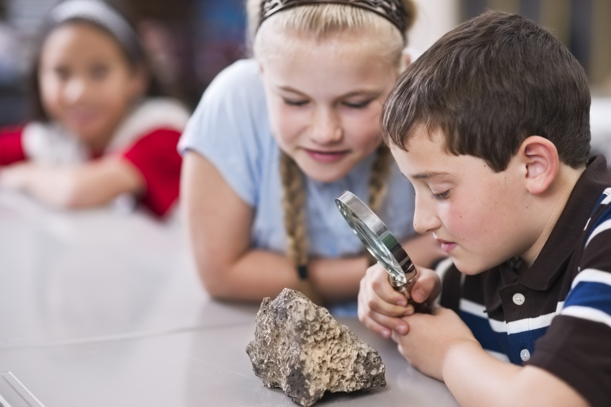Children using a magnifying glass to get a close look at a small boulder.