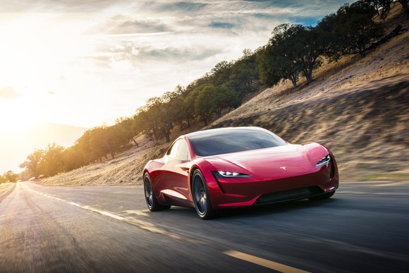 Red Tesla Roadster in motion as the sun rises.