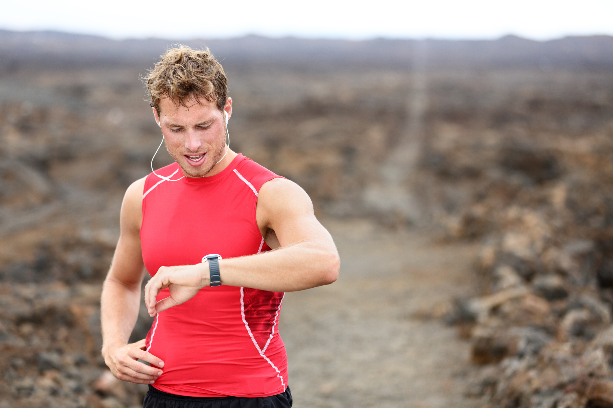 Trail runner in red tank top checking sports watch.