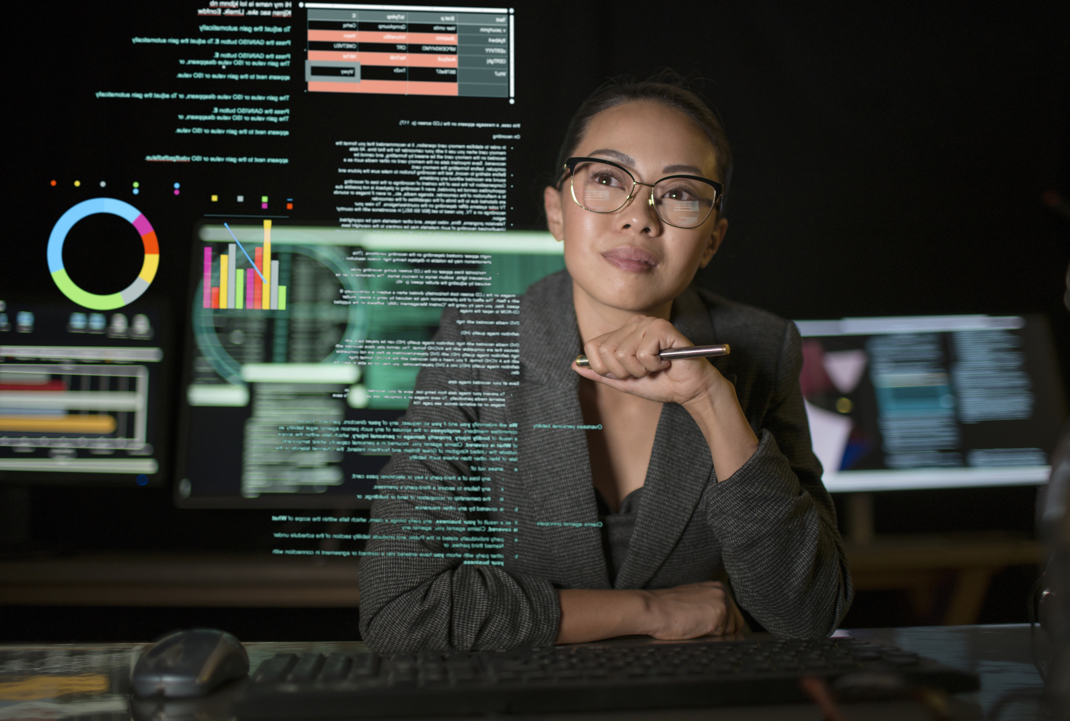 Female software engineer looks at a translucent screen with graphs and data on it in a dark room.