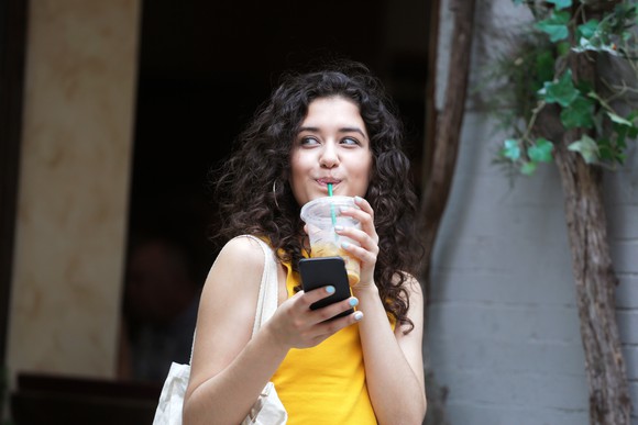A woman drinking coffee while holding her phone.