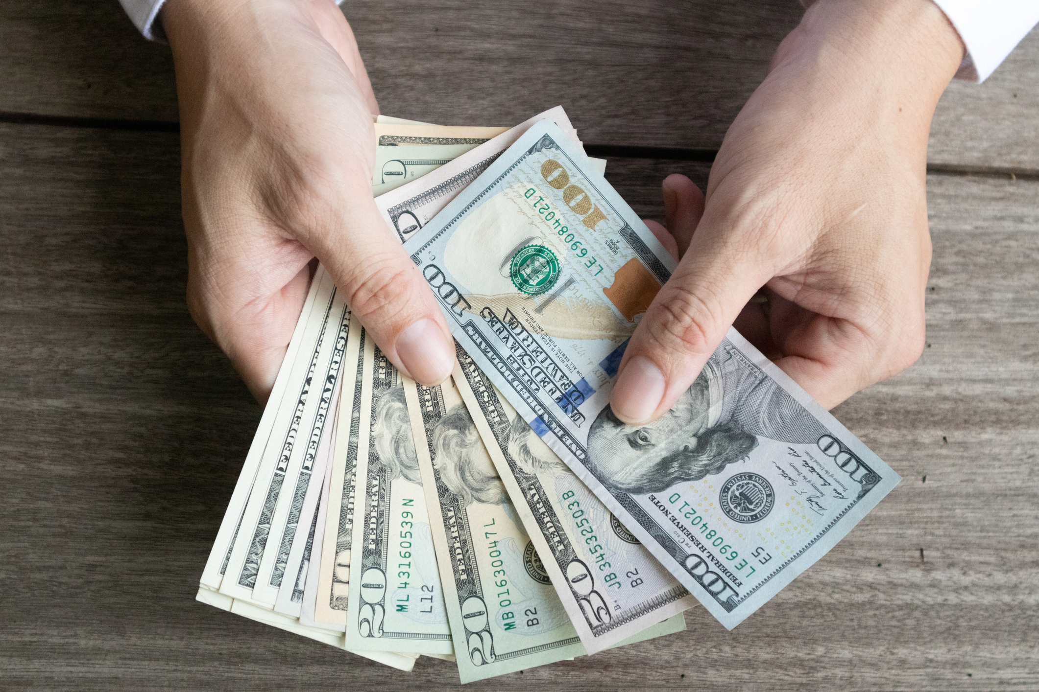 A person counting a fanned pile of assorted cash bills.