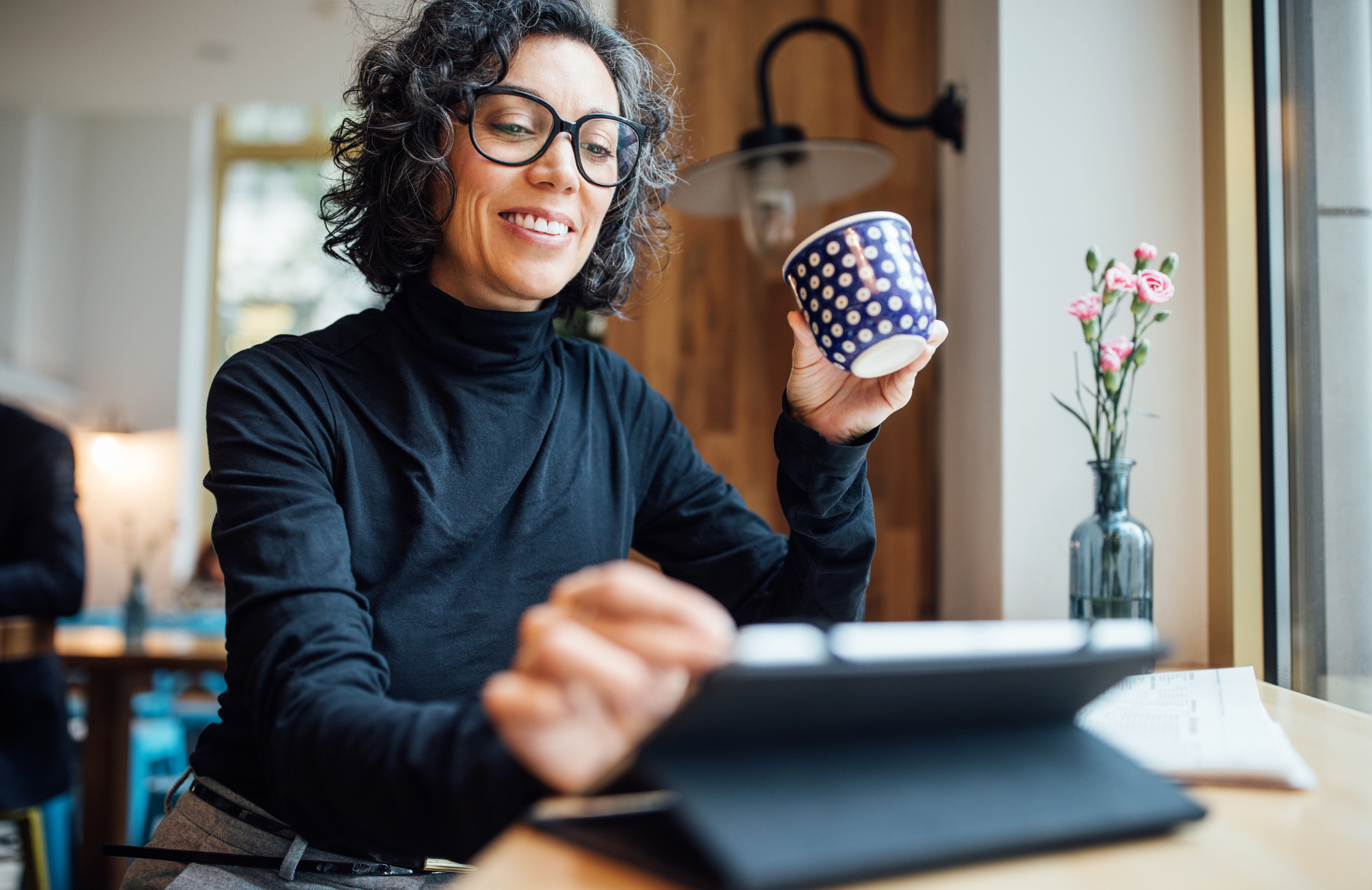 A smiling person holding a coffee cup and looking at a touchscreen tablet.