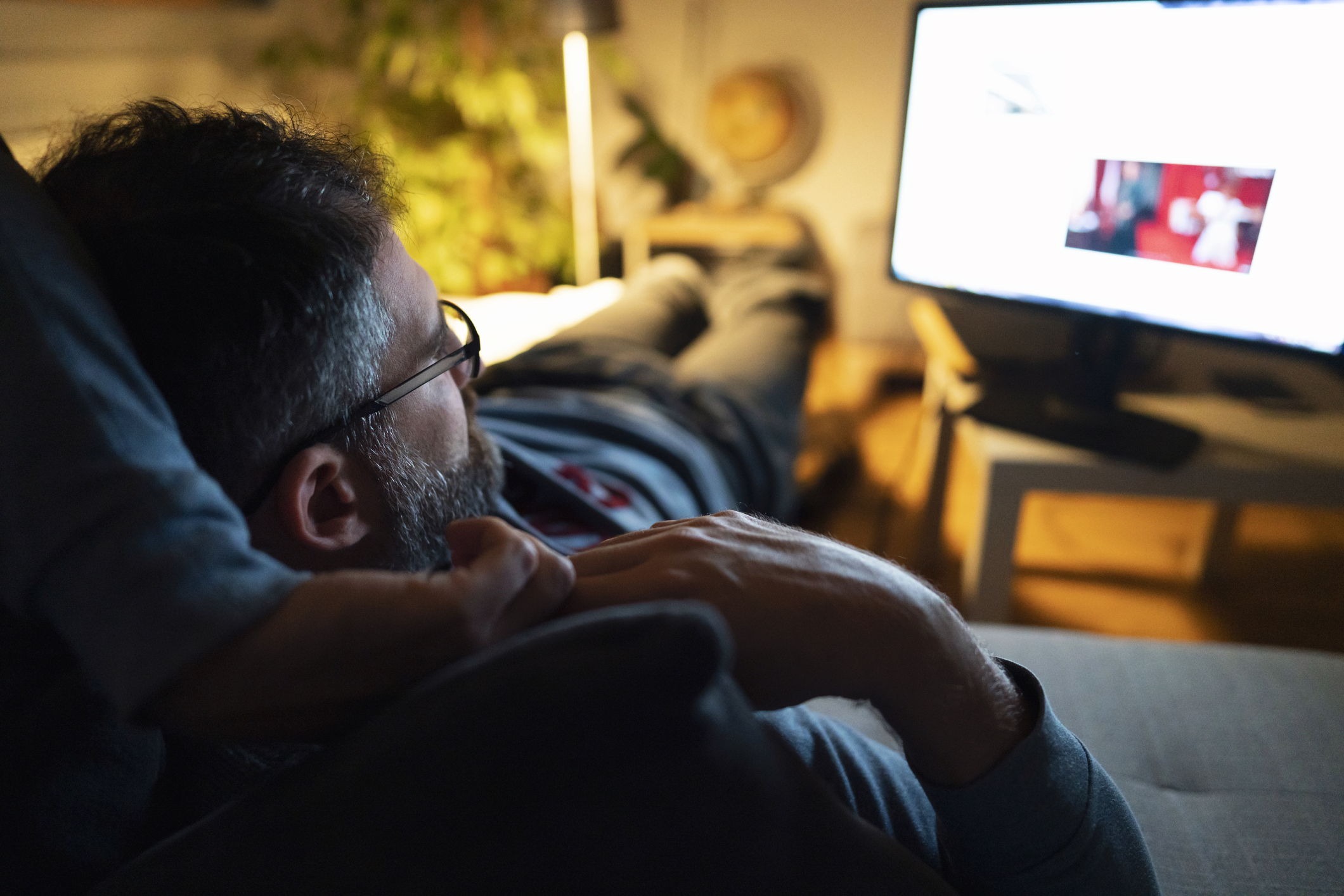 A relaxed middle-aged person watching TV at home.