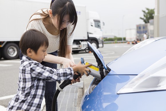 Adult and child charging electric vehicle at station.