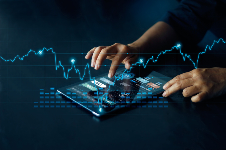Dark background with an electric-blue graph line crossing its length. In the middle is a set of hands using a tablet.