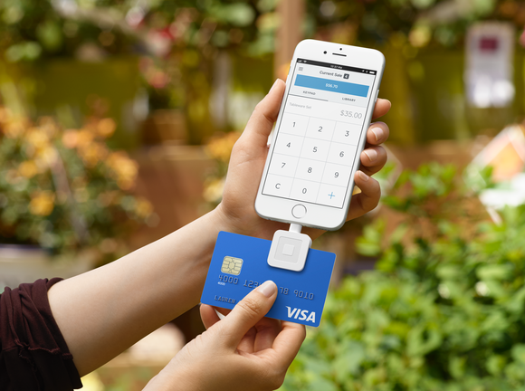 A person swiping a credit card through a Square card reader that's plugged into a smartphone.
