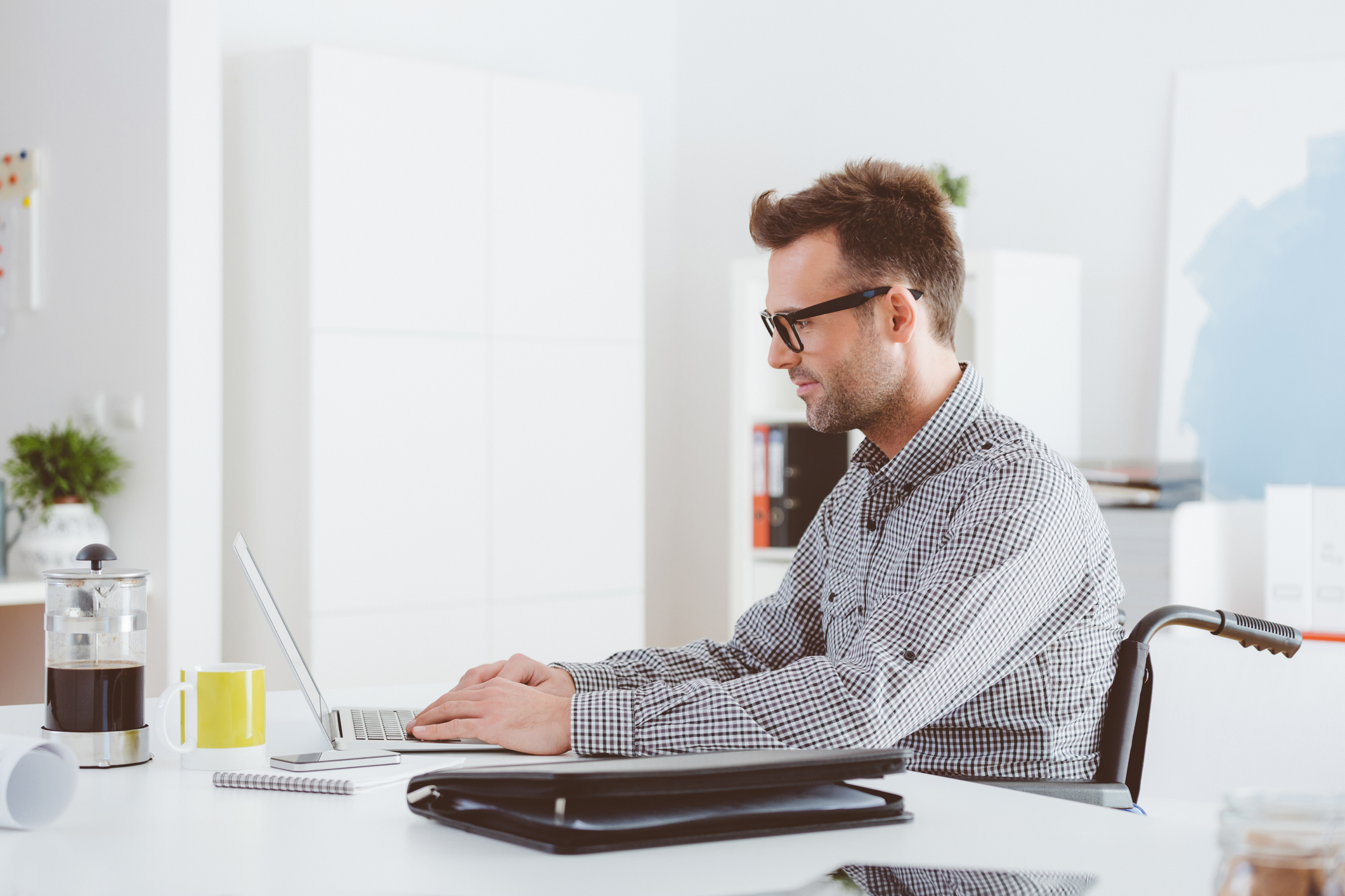 An investor who uses a wheelchair studies something on a laptop in an office setting.