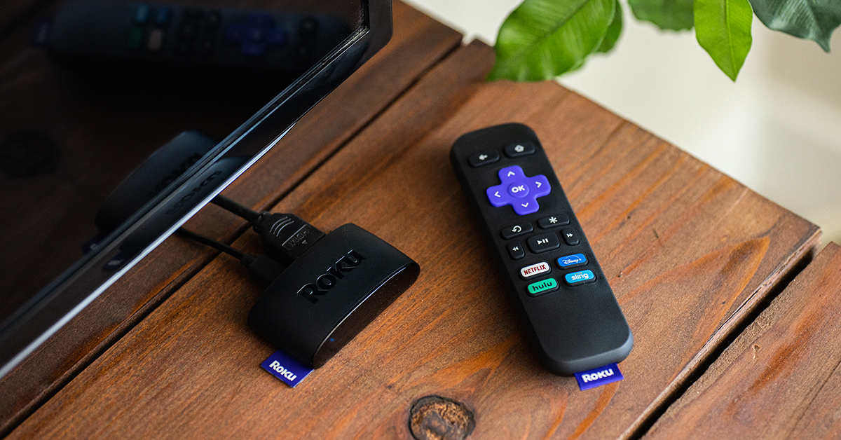 A Roku remote sitting on a table next to a Roku player.