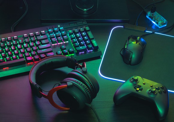 A controller, mouse, keyboard, and gaming headset spread out on a desk.
