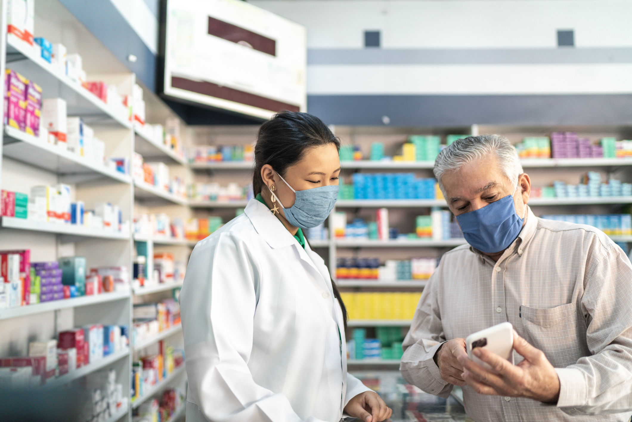 A pharmacist helps a customer with a question while standing behind the counter at the pharmacy.