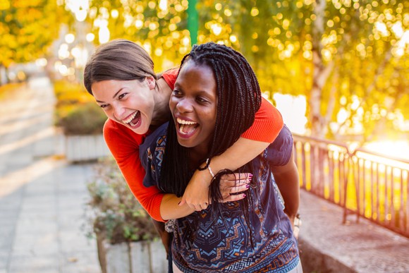 Two people outdoors, hugging, smiling and laughing.