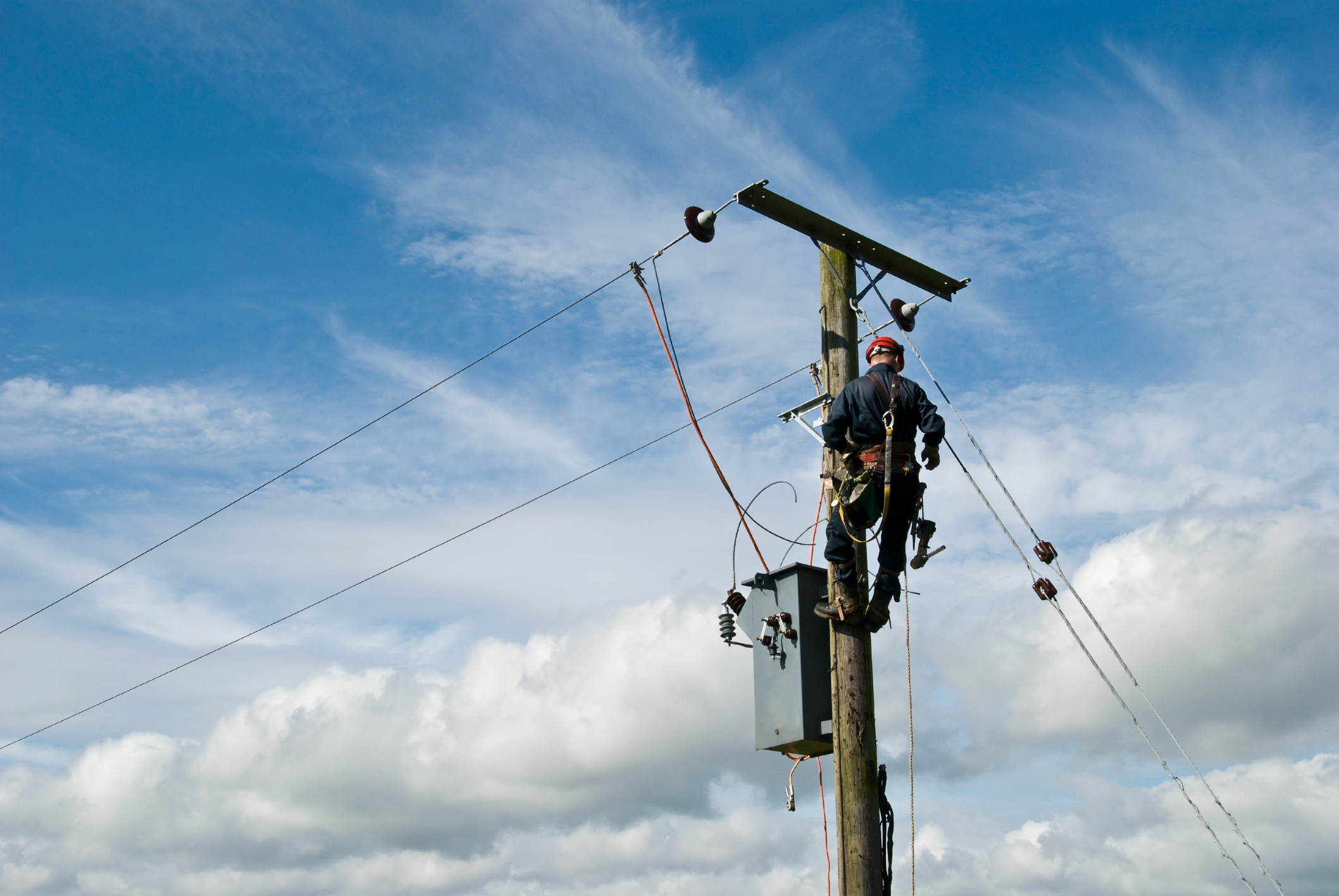 A utility worker repairs a transformer on a power line.