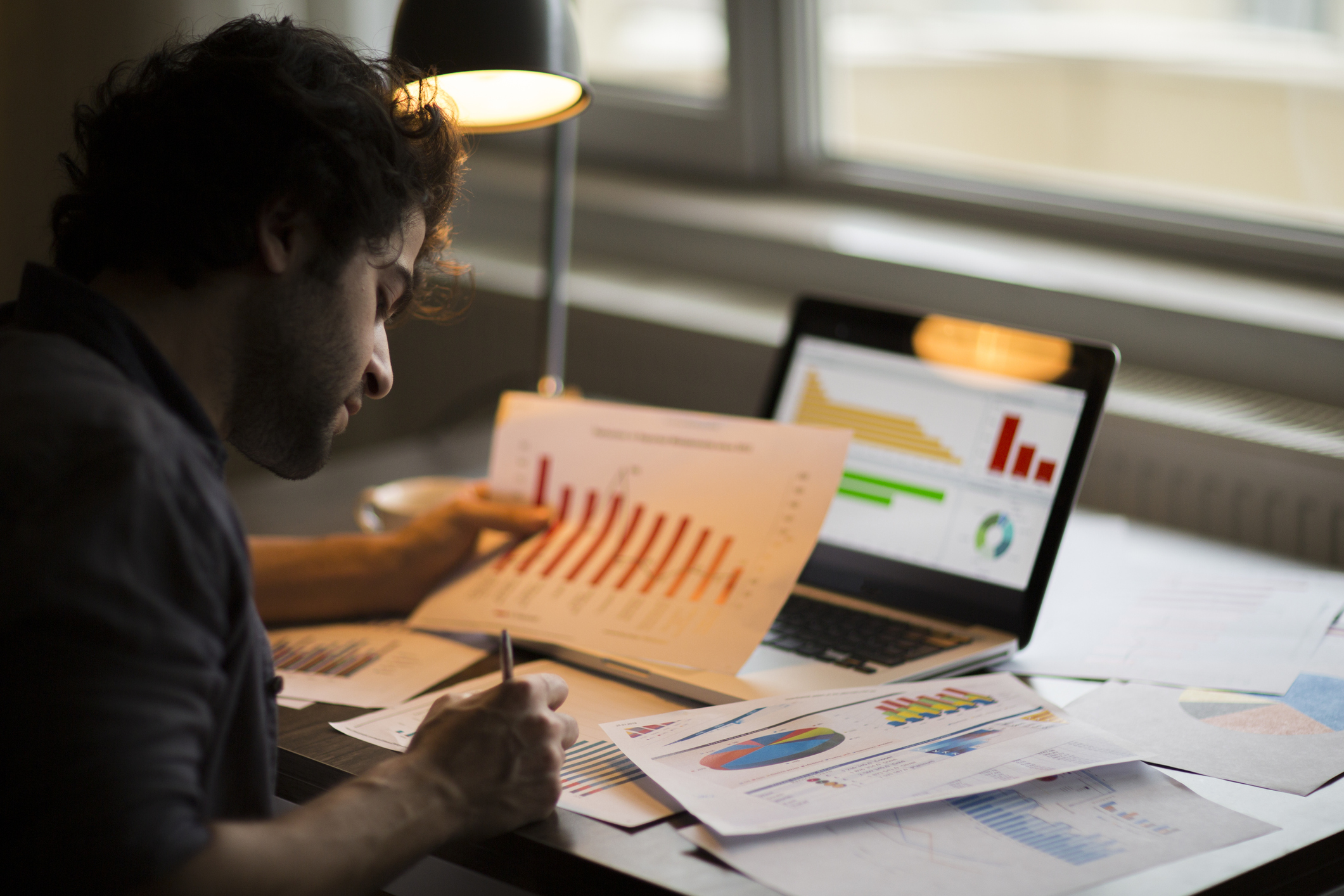 Investor studying various chart and graphs, both on paper and a digital tablet.