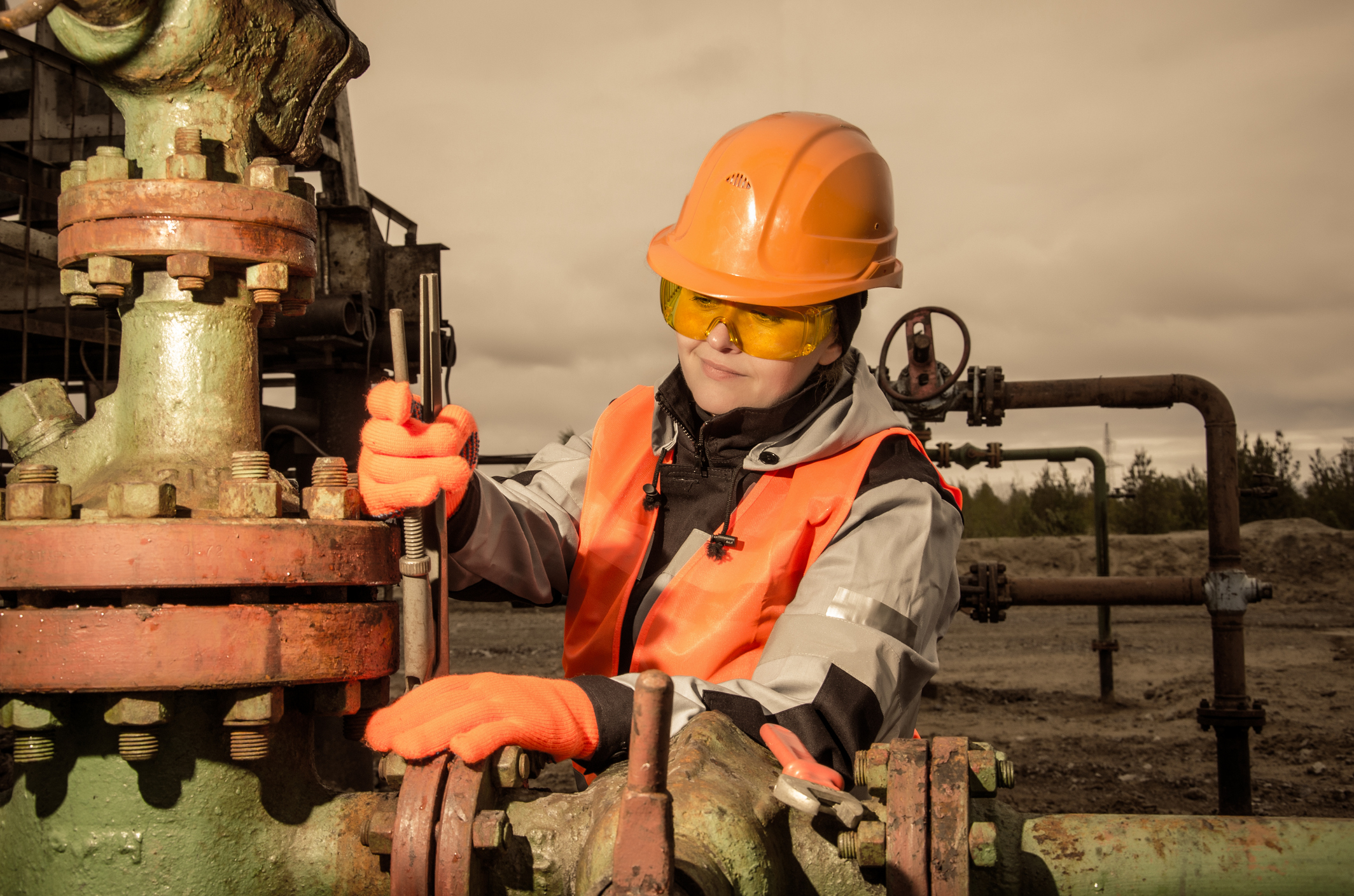 Worker wearing orange hard hat working near oil pump equipment.