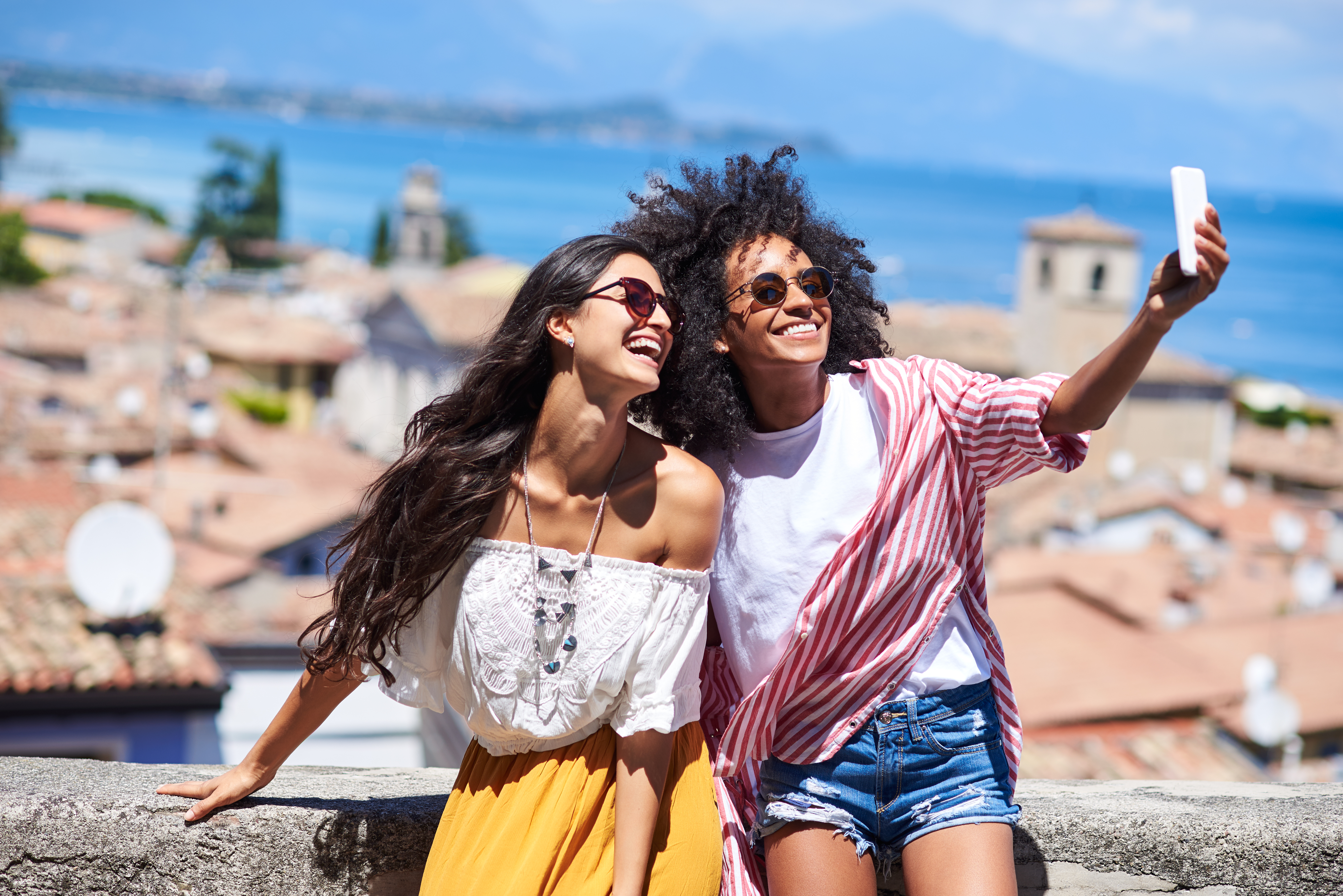 Two excited friends taking a selfie in a sunny European location.