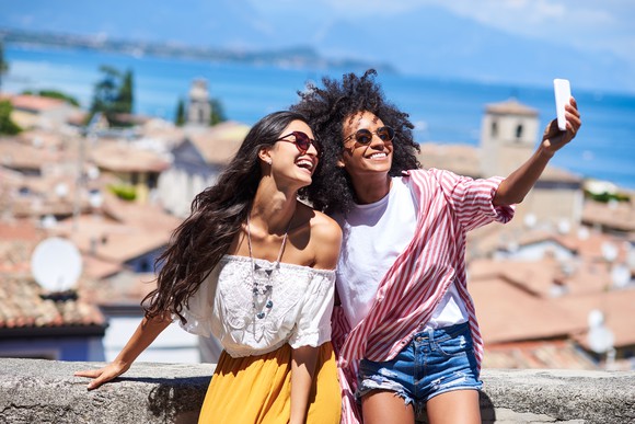 Two excited friends taking a selfie in a sunny European location.