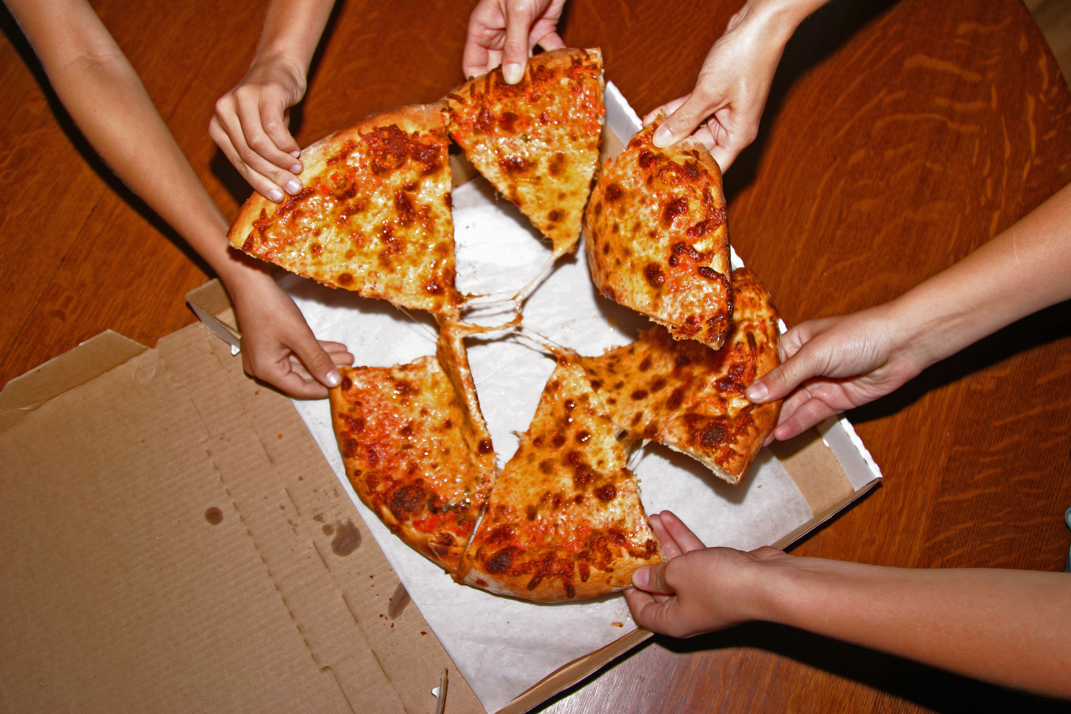 People taking slices of cheese pizza out of a pizza box.