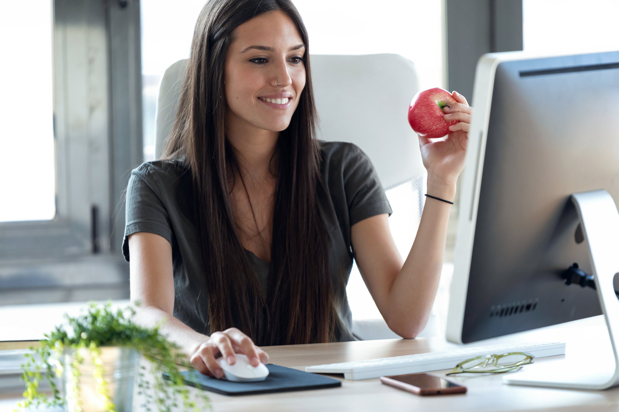 Person sitting at a desk in front of a monitor holds an apple.