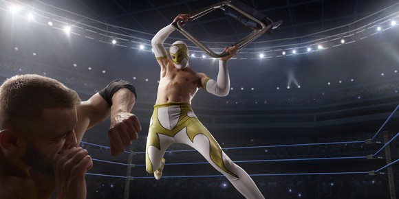 A masked professional wrestler about to attack a rival with a chair in the ring during a performance.