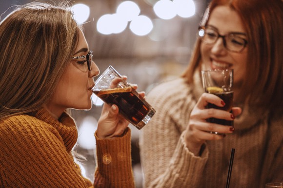 Two young people drinking soda while sitting together.