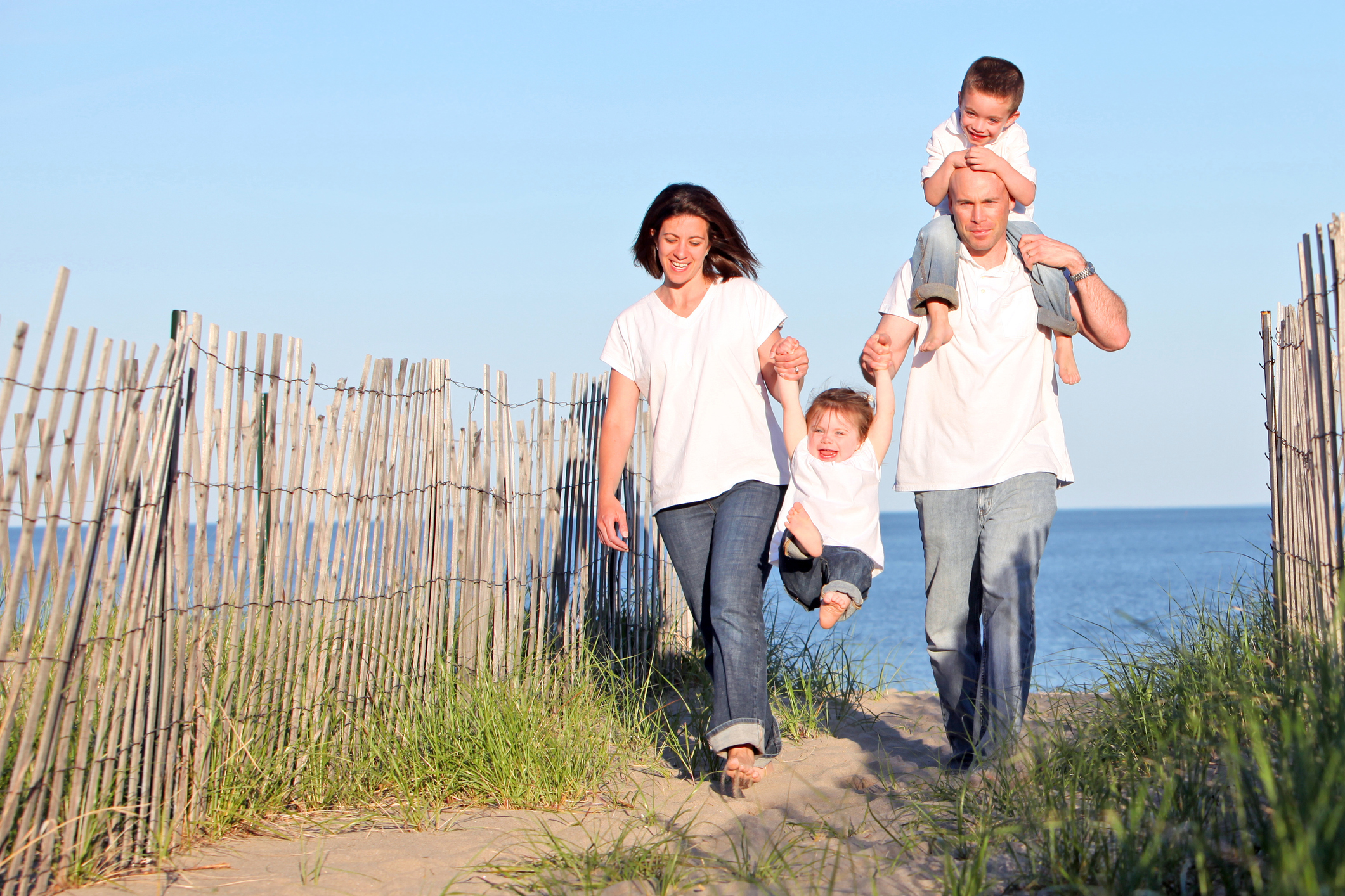 A family with children -- all dressed in jeans and white t-shirts -- walking on beach.