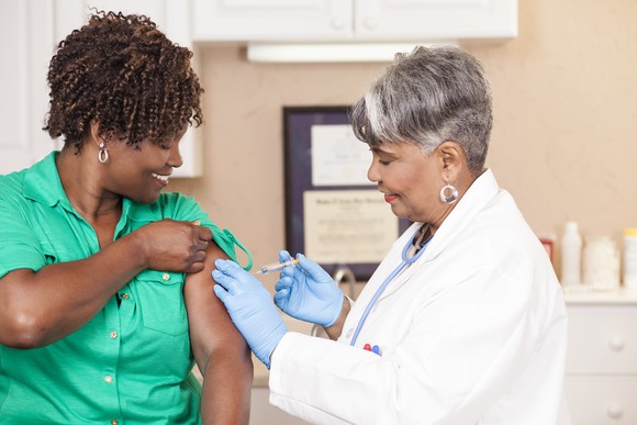 A physician administering a vaccine into the upper left arm of a patient.