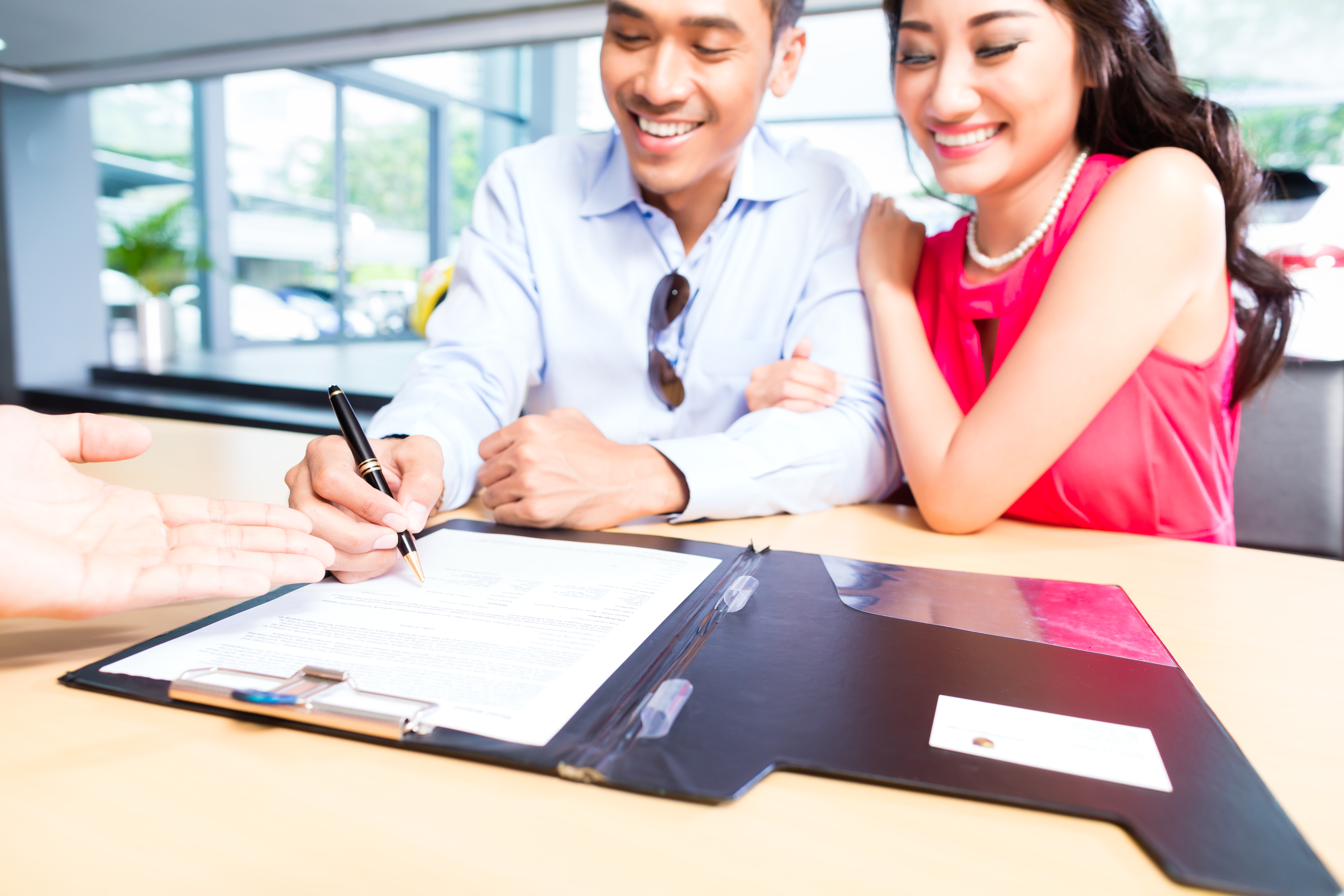 A smiling couple signing sales contracts at a car dealership.